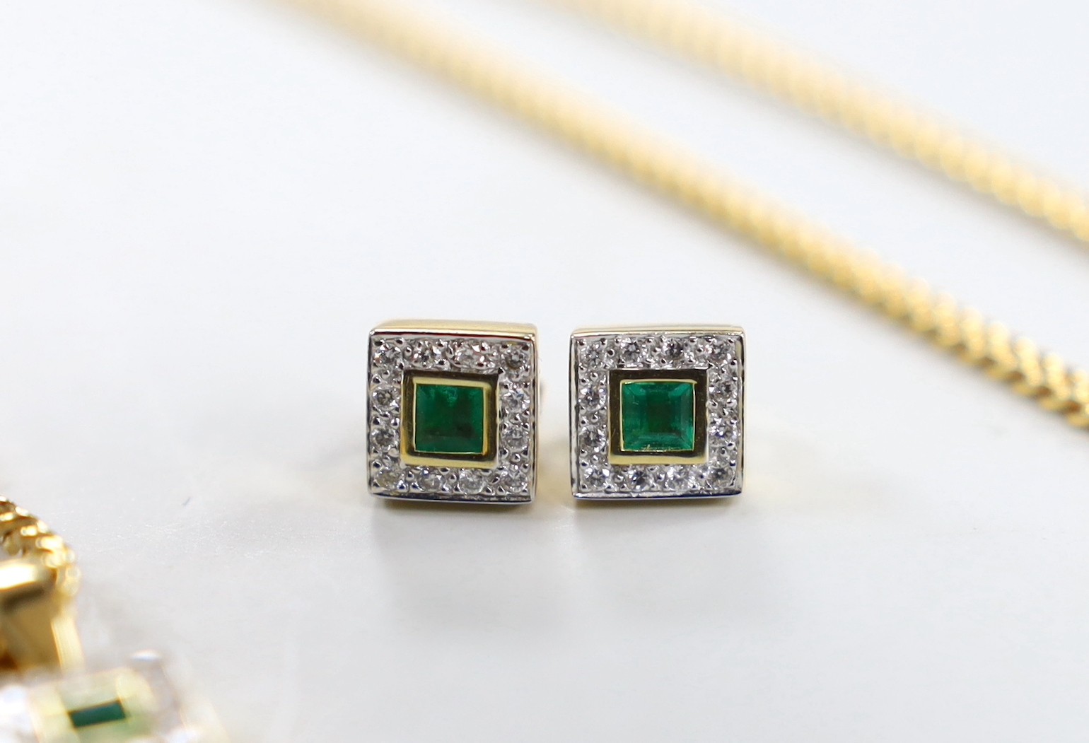 A modern 18ct gold, emerald and diamond set square cluster pendant, 7mm and a pair of matching ear studs, gross weight 4.6 grams, the pendant with an associated 9ct chain, 50cm, 8.6 grams.